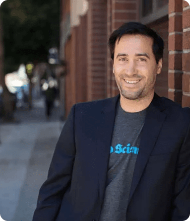 A man in a suit and tie stands confidently in front of a textured brick wall, representing professionalism and expertise.