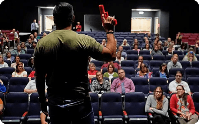 A man demonstrates active shooter response techniques with a gun in front of an audience during a training program.