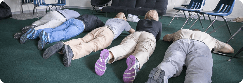 A group of people practicing active shooter response techniques by laying on the floor during a training session.