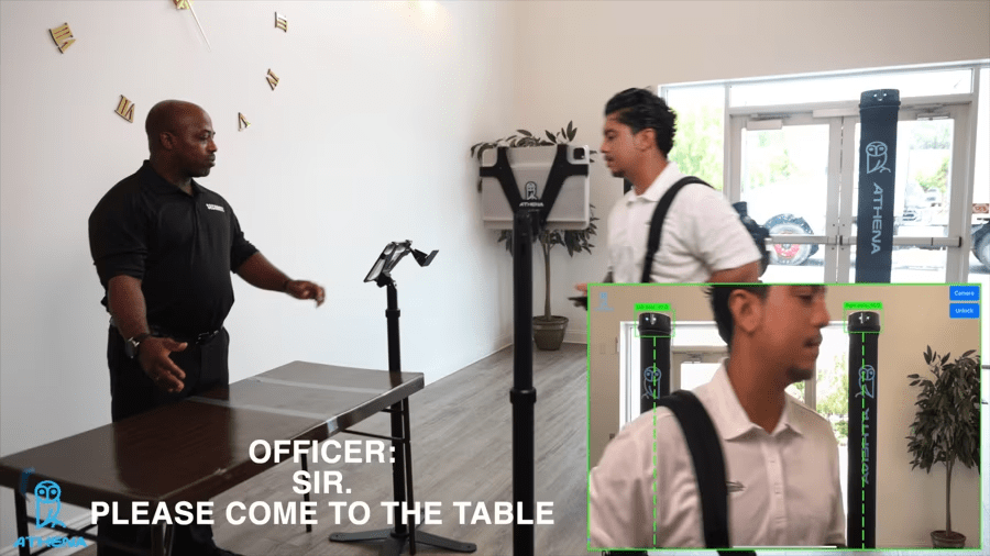 Two men stand by a table featuring an advanced AI weapons detection system, showcasing its hardware-agnostic capabilities.