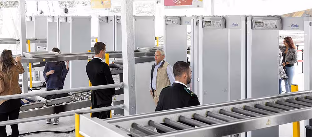 CEIA HI-PE Plus walk-through metal detectors in busy security screening area with people, conveyor belts, and inspection lanes indoors