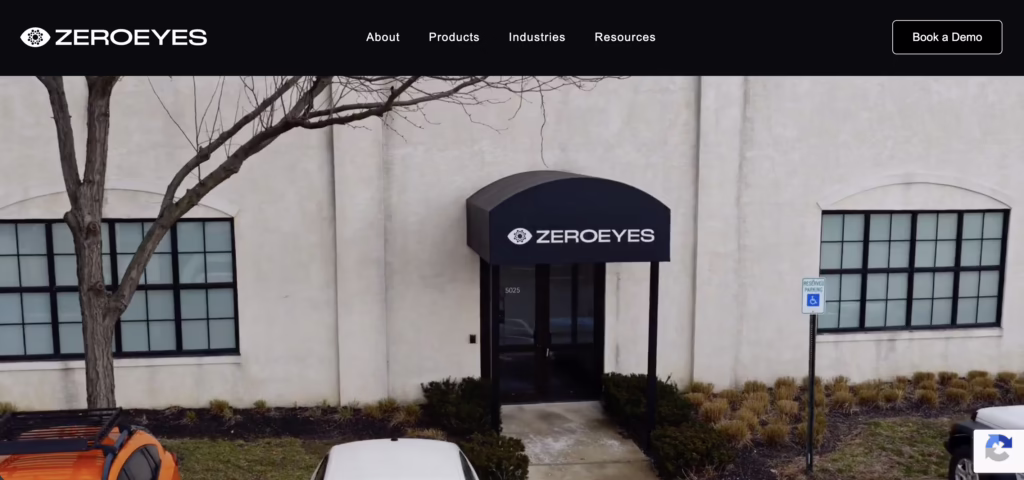  ZeroEyes office entrance with black branded awning, glass door, beige exterior walls, and parking area with trees and signage